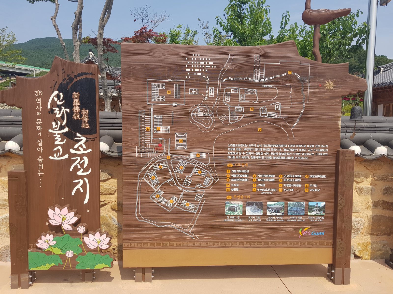 나무 안내판 — 왼쪽에 붓글씨 «신라불교초전지» 판과 연꽃 그림, 오른쪽에 배치도